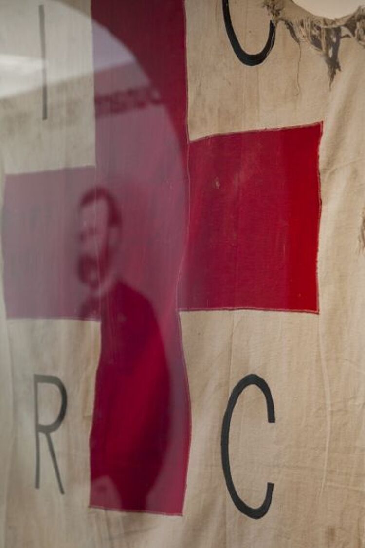 Im Henry-Dunant-Museum im schweizerischen Heiden spiegelt sich sein Porträt in einer Vitrine mit einer zerschlissenen Rotkreuzfahne, die während des Bürgerkriegs in Angola benutzt wurde (Jörg F. Müller / DRK) Im Henry-Dunant-Museum im schweizerischen Heiden spiegelt sich sein Porträt in einer Vitrine mit einer zerschlissenen Rotkreuzfahne, die während des Bürgerkriegs in Angola benutzt wurde (Jörg F. Müller / DRK)